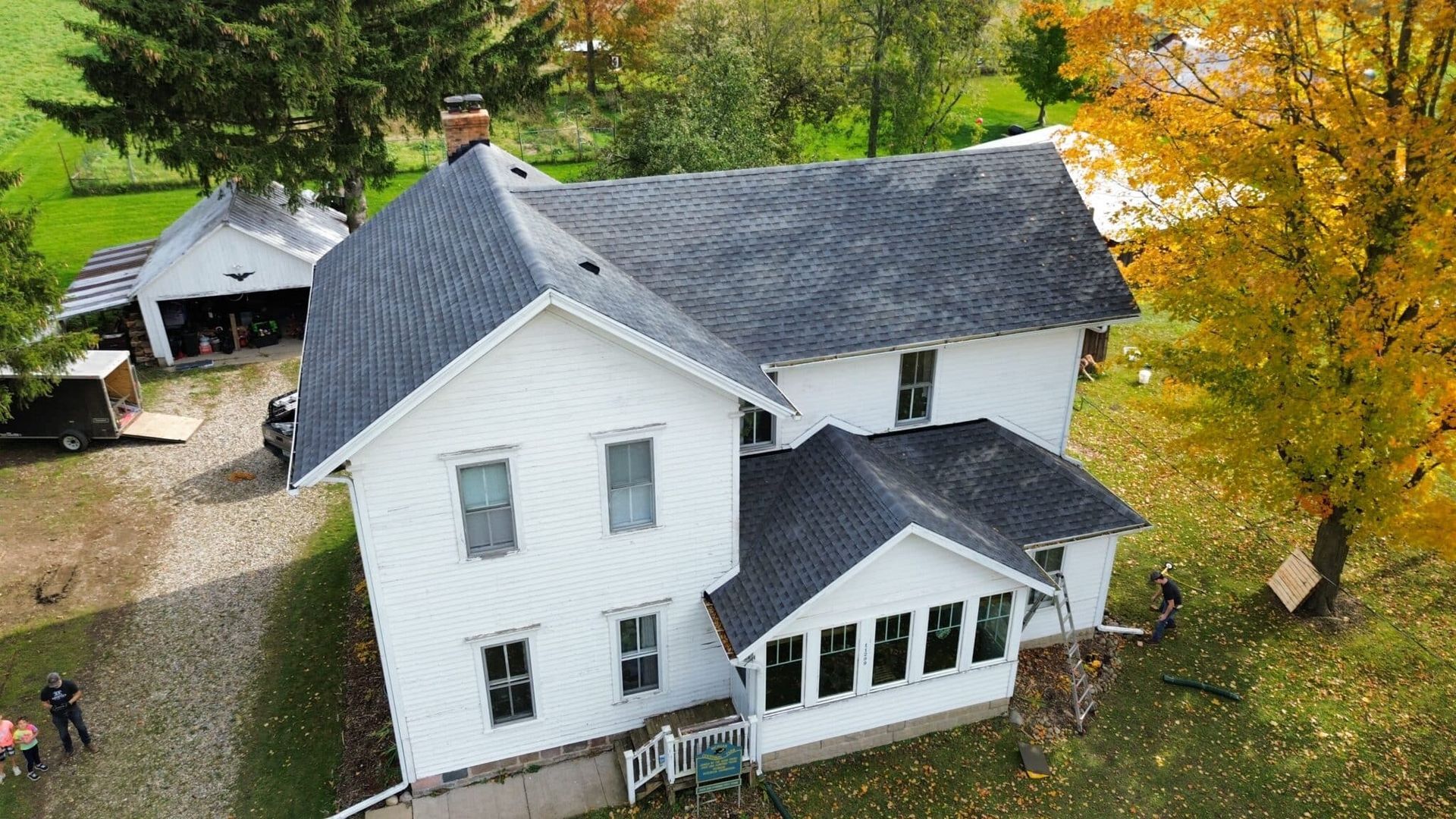 White house with gray roof, sunroom, and chimney, on a grassy lot with fall foliage.