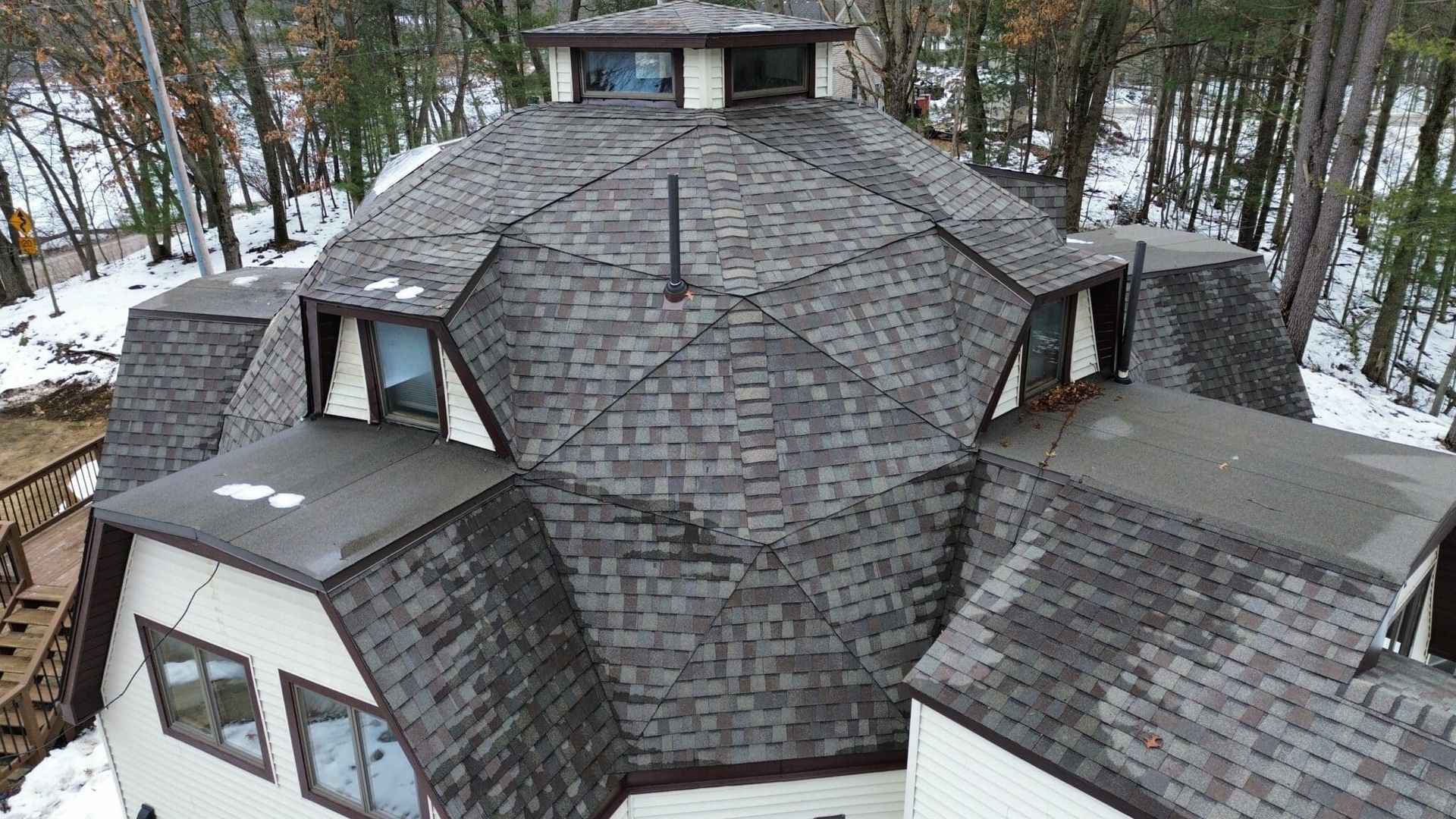 Dome-shaped house with a dark gray roof, surrounded by trees and patches of snow.
