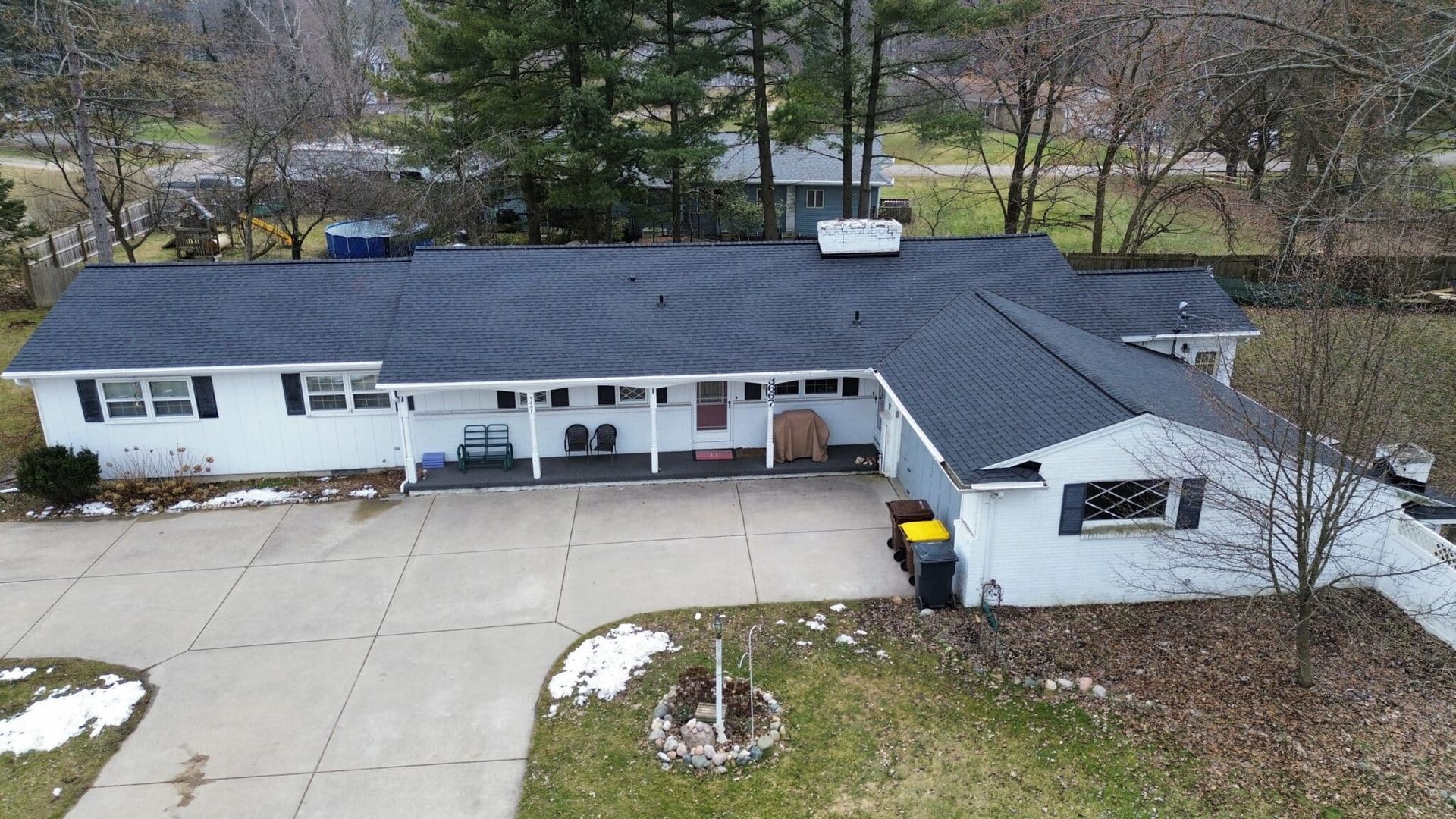A white ranch-style house with a dark roof and a long concrete driveway on a cloudy day.