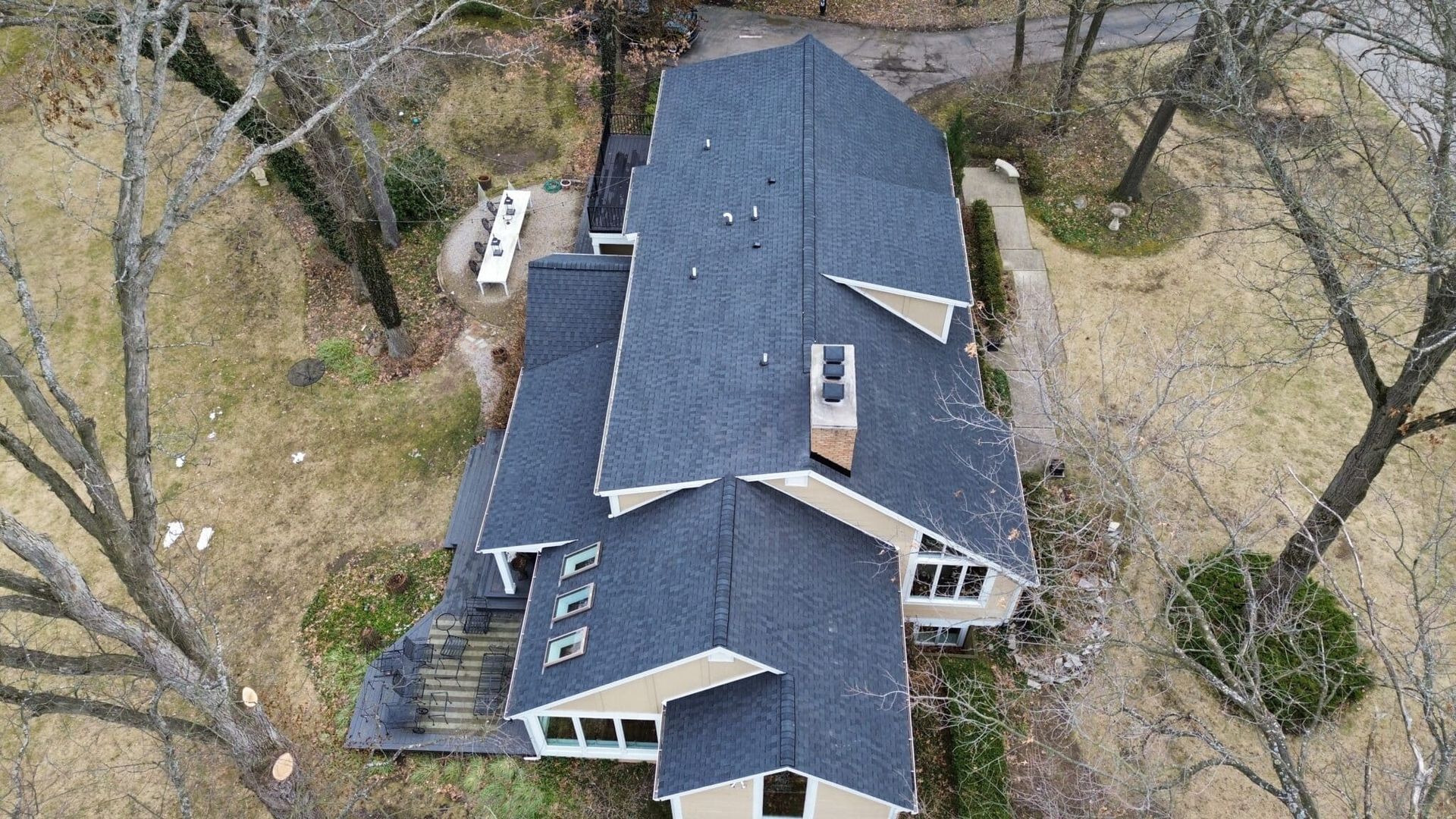 Overhead view of a house with a dark roof and beige siding, surrounded by trees.