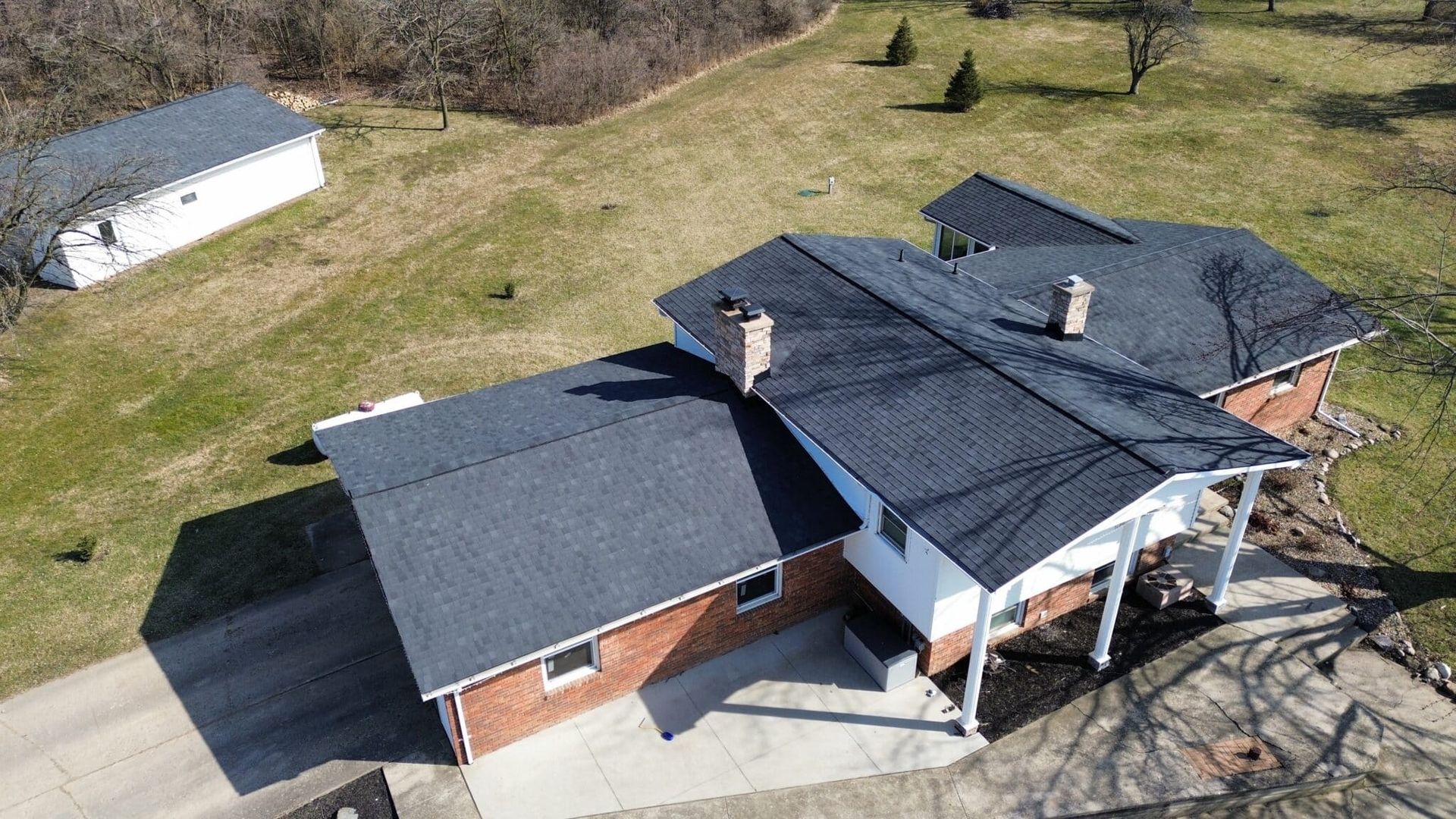 Aerial view of a house with a dark roof and a small building, set in a grassy yard.