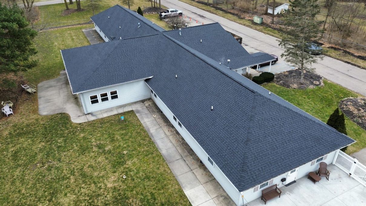 Aerial view of a gray-roofed house with a long driveway and surrounding green grass.
