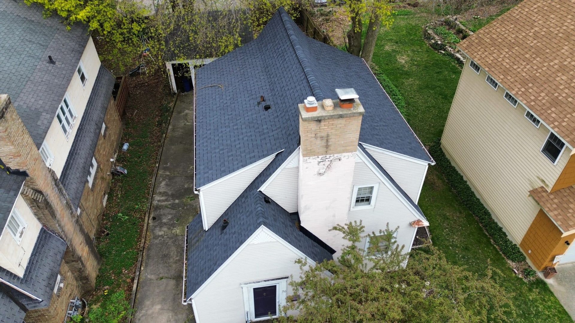 Overhead view of a white house with a dark gray roof and a chimney, located between two other houses.