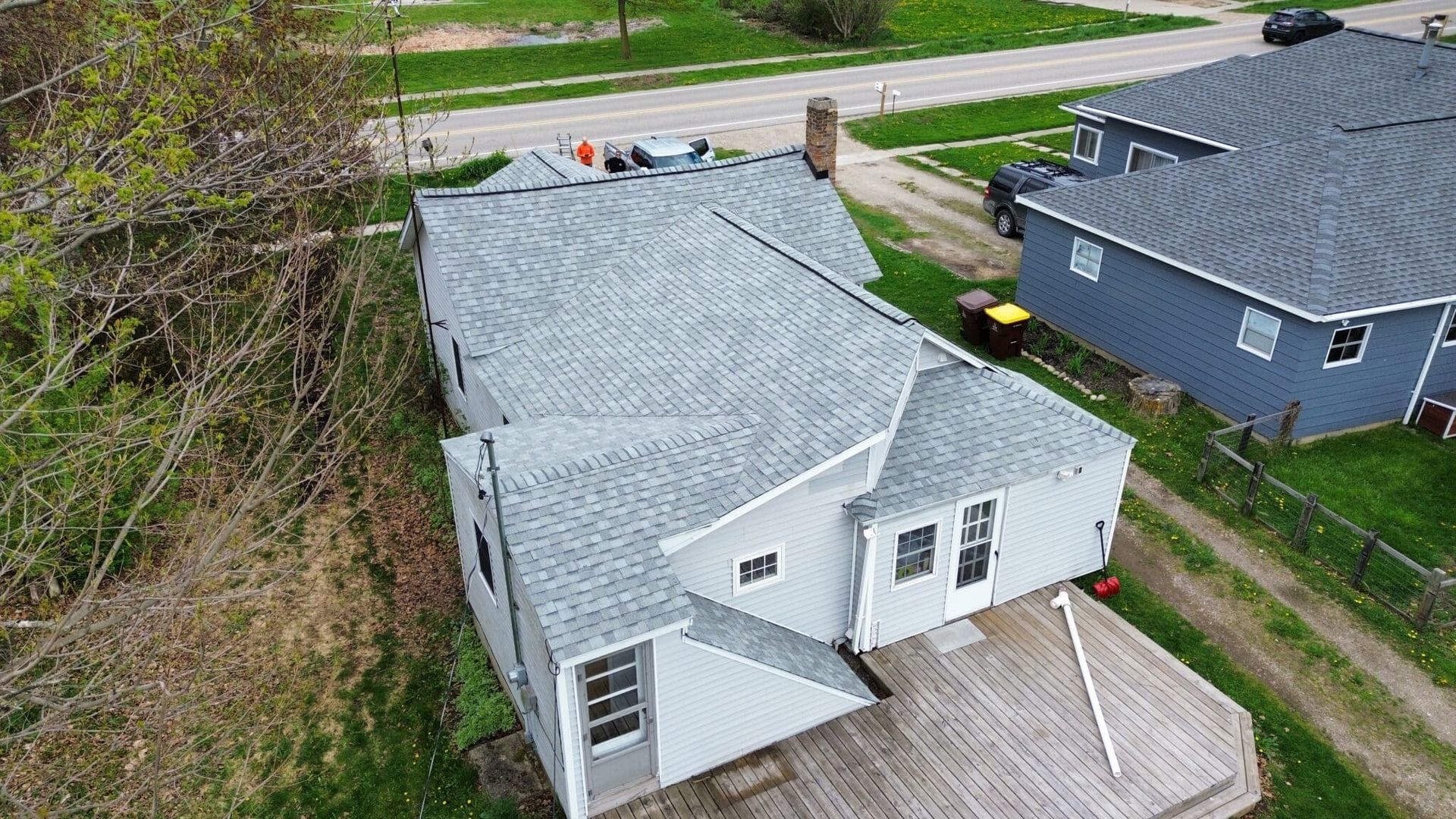 Overhead view of a house with a gray roof, a deck, and a driveway next to a grassy area.