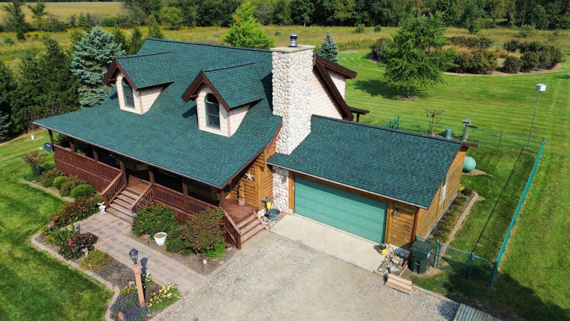 Two-story house with green roof, attached garage, and stone chimney on grassy property.