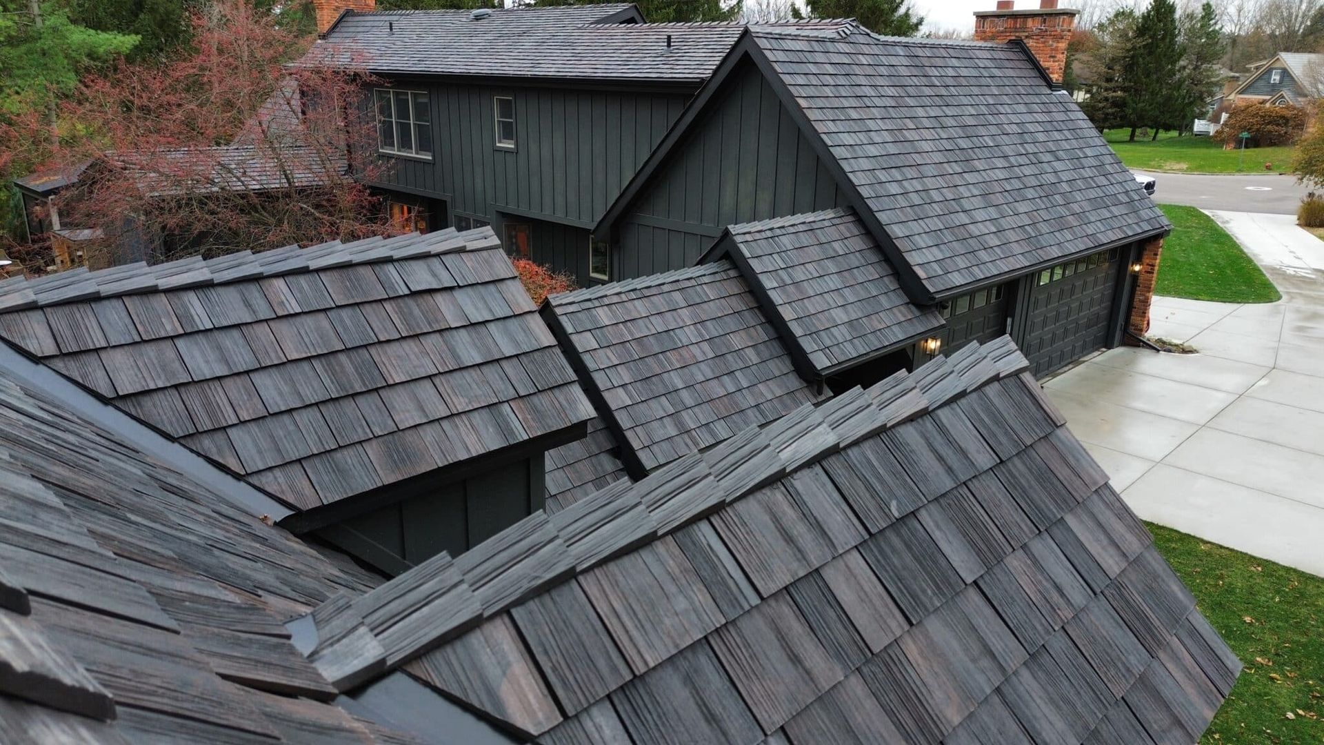 Dark gray shingle roof on a multi-level house with a brick chimney and a driveway.