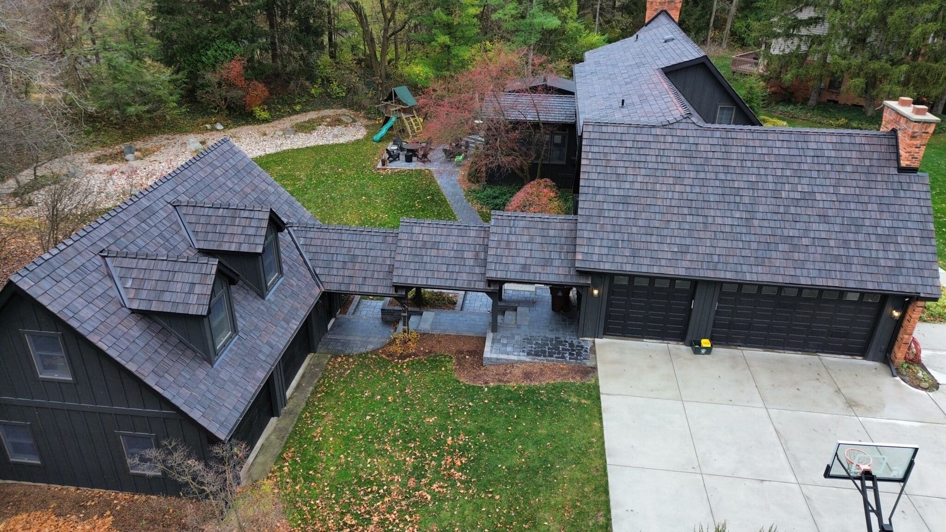 Black house with multiple roof levels, a driveway, and autumn foliage.