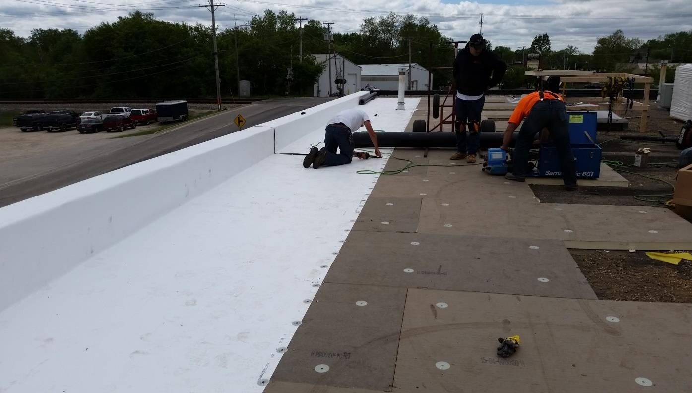 Roofing workers installing a white membrane on a flat roof.