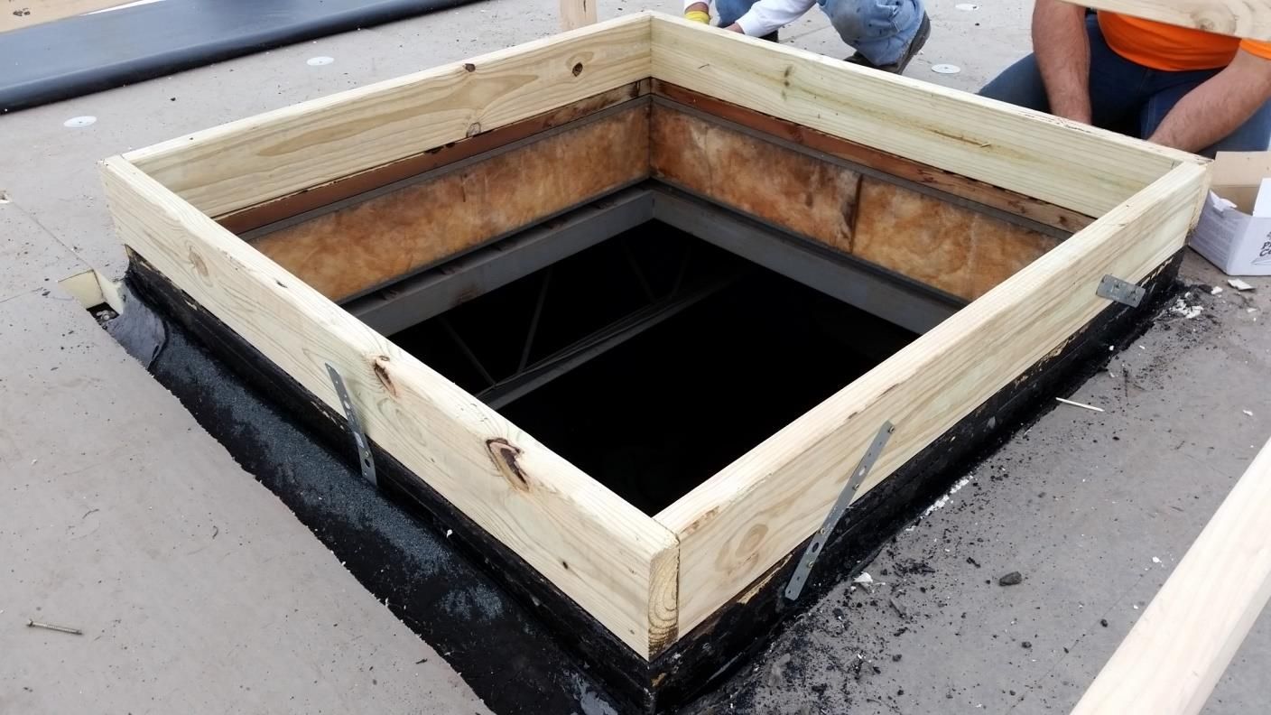 Wooden frame around a roof opening, black tar around base, construction site.