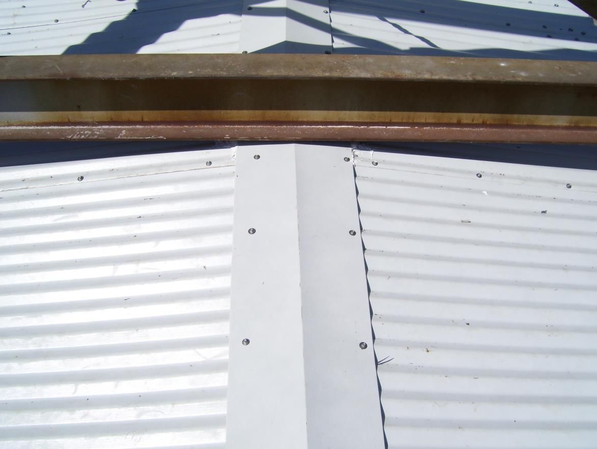 Close-up of a metal roof peak with white flashing and corrugated panels.