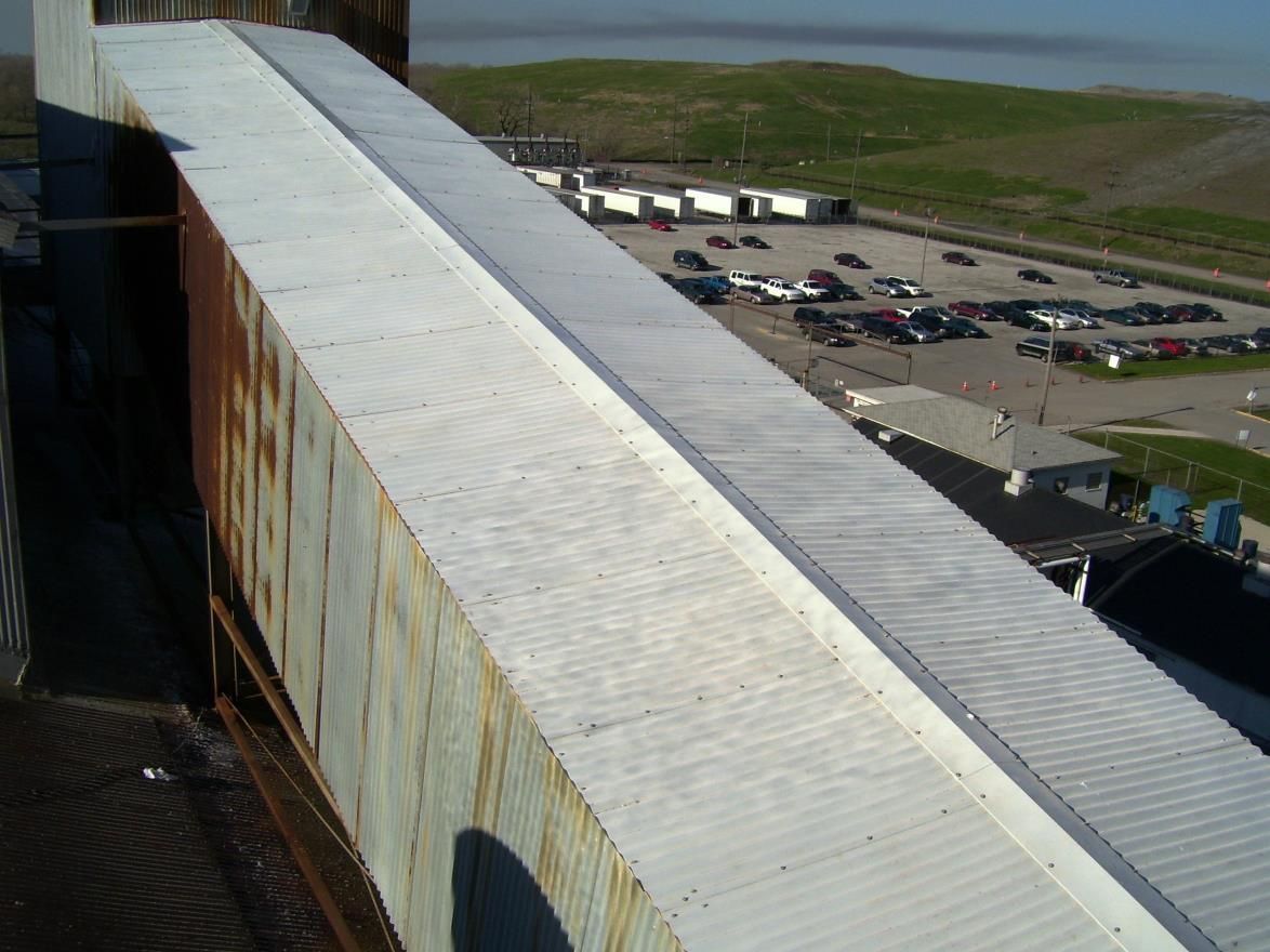 Elevated walkway with metal siding, leading to a parking lot and industrial buildings.
