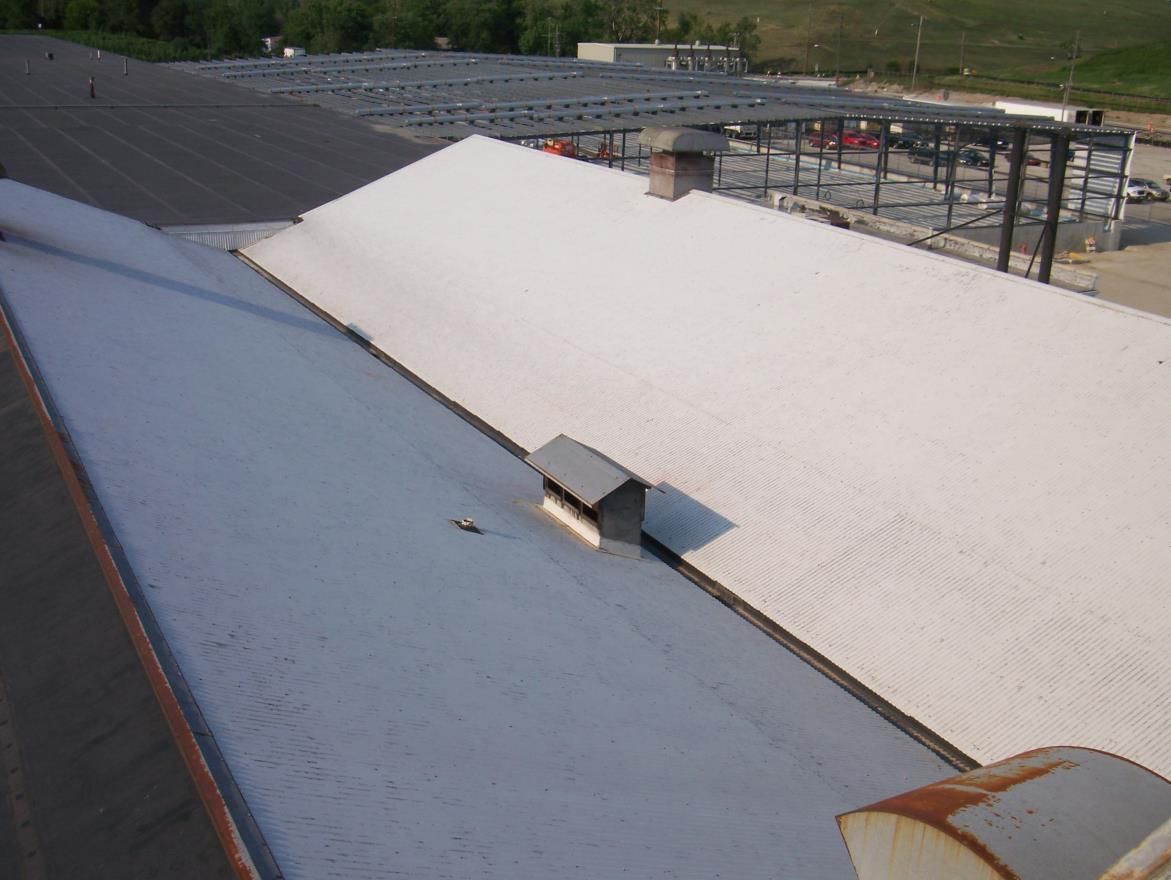 Overhead view of corrugated metal roofs, gray and white, with a chimney and building under construction in the background.