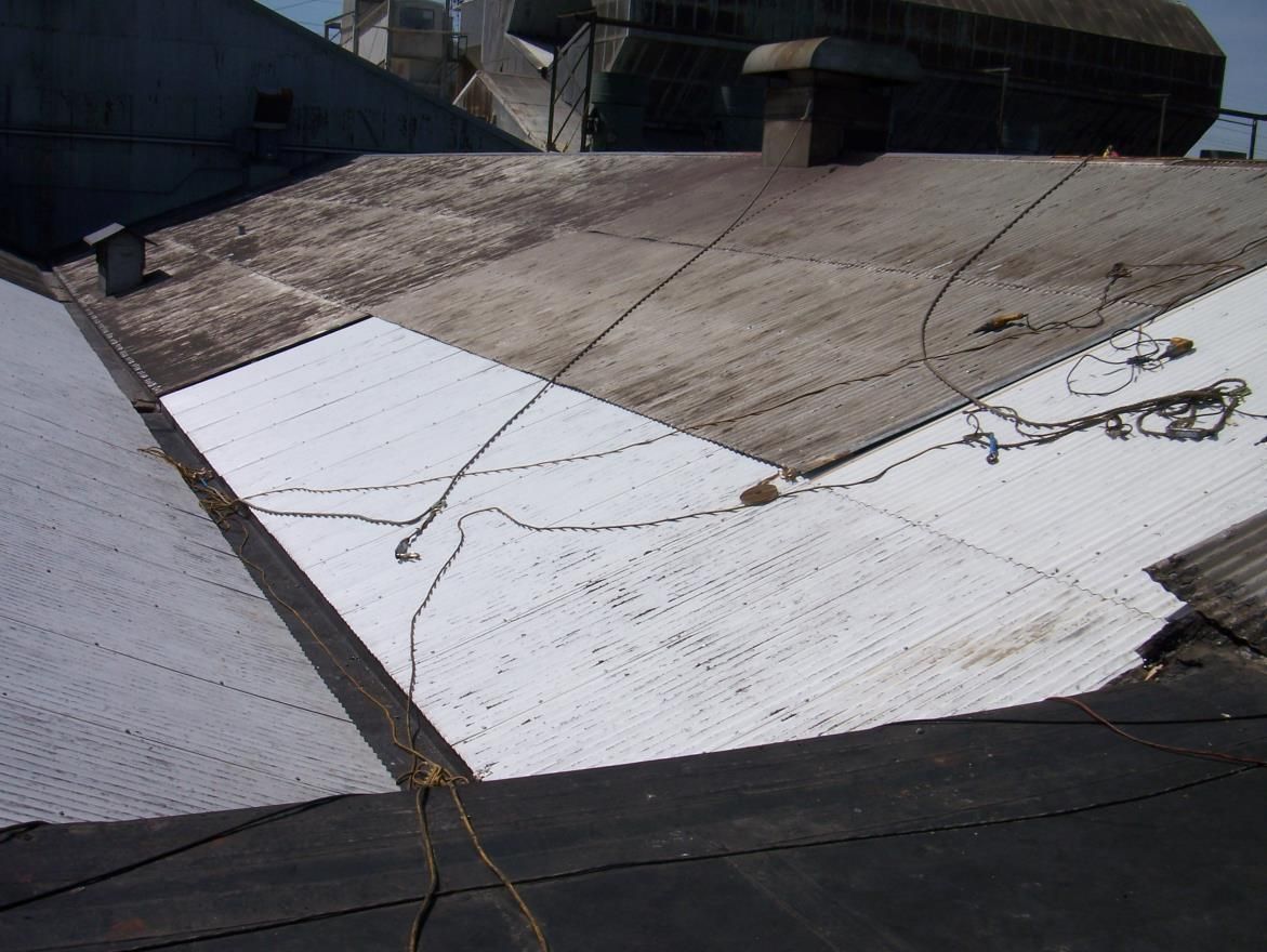 View of a weathered, multi-paneled rooftop, part white, part dark, with wires strung across.