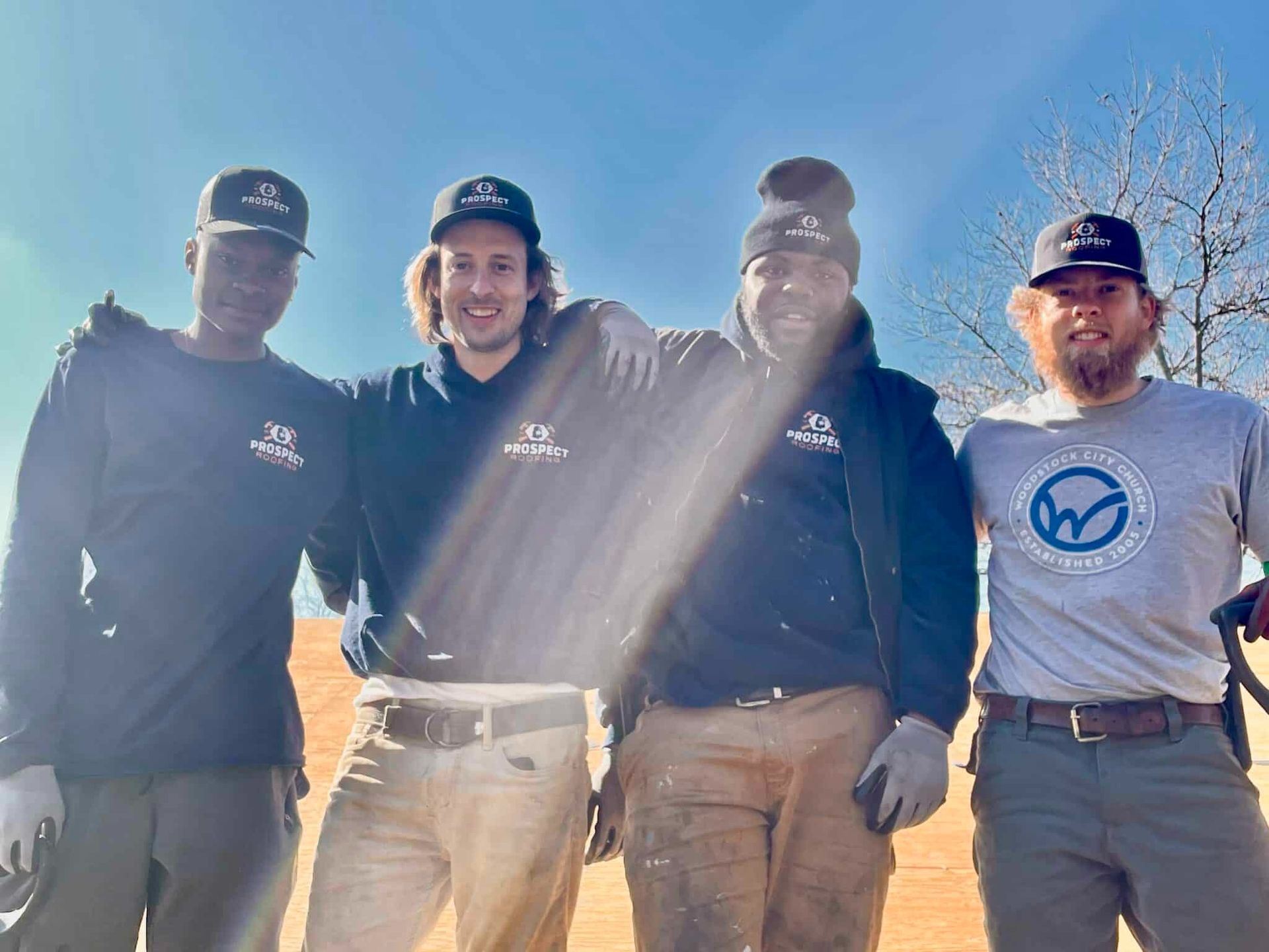Four people in work clothes smile at the camera outdoors under a bright sky.