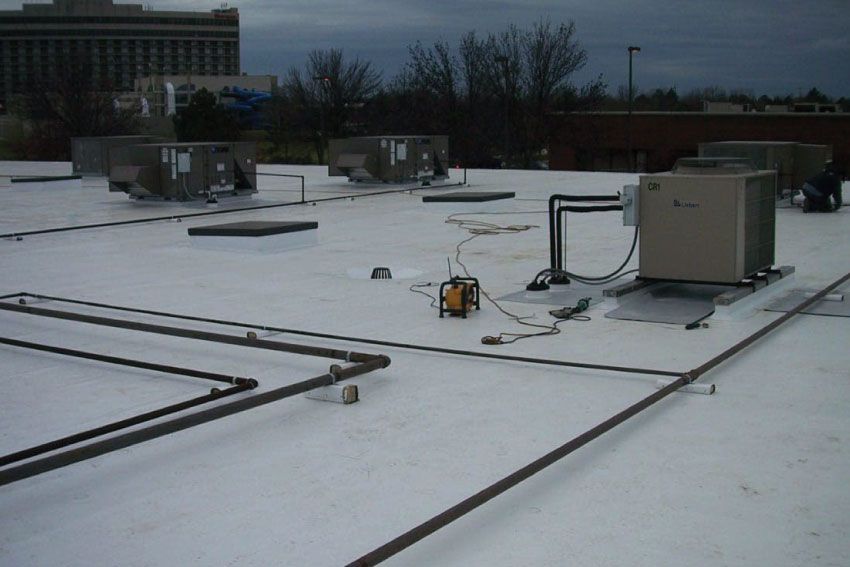 HVAC units and piping on a flat commercial roof, overcast sky.