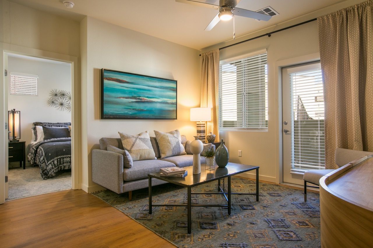Living room in an apartment with a sofa, coffee table, rug, lamp, and balcony door.