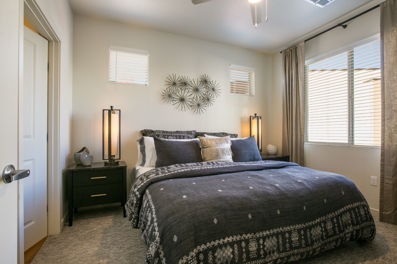 Bedroom with a large bed, two nightstands, two tall lamps, and a window with blinds.