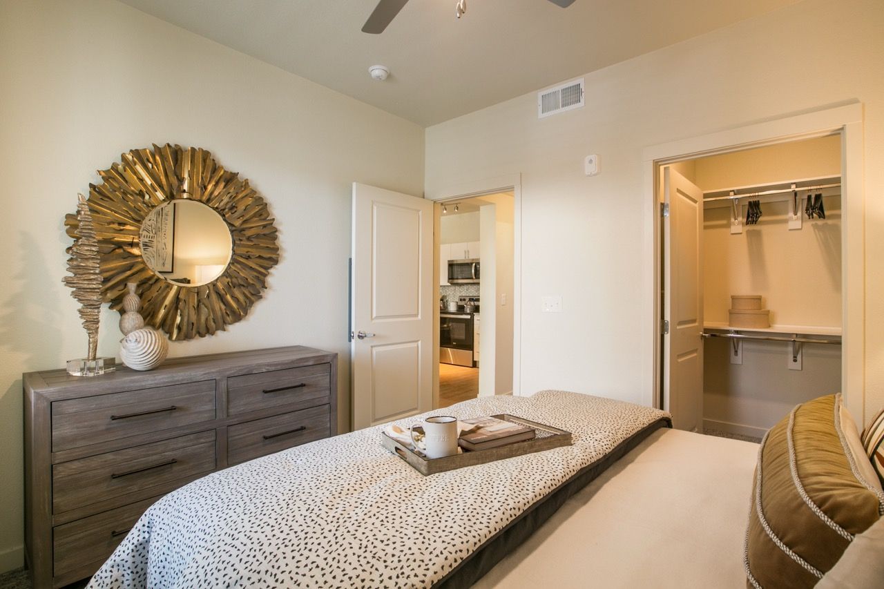Bedroom in an apartment with a bed, dresser, round sunburst mirror, and open closet.