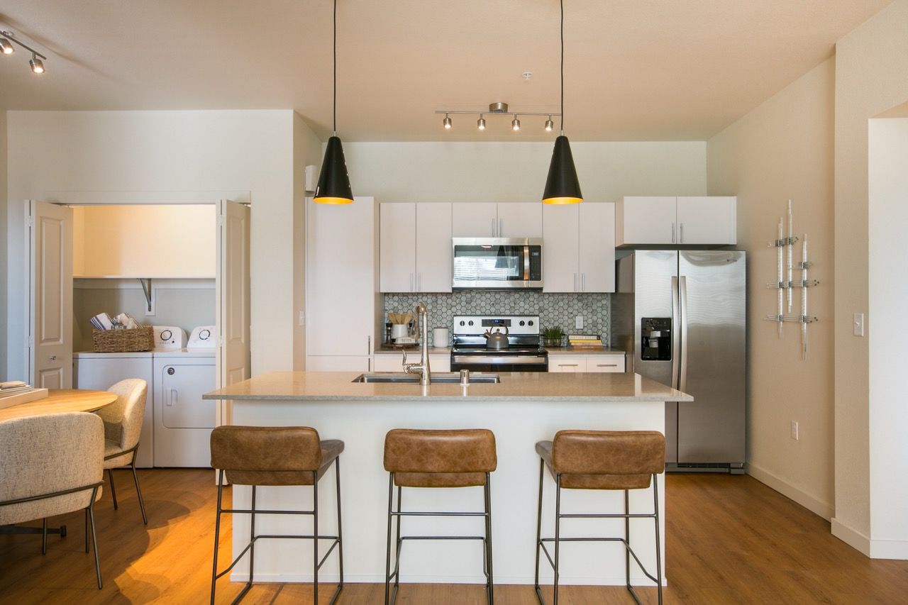 Modern open-concept kitchen with island, white cabinets, stainless appliances, and three bar stools.