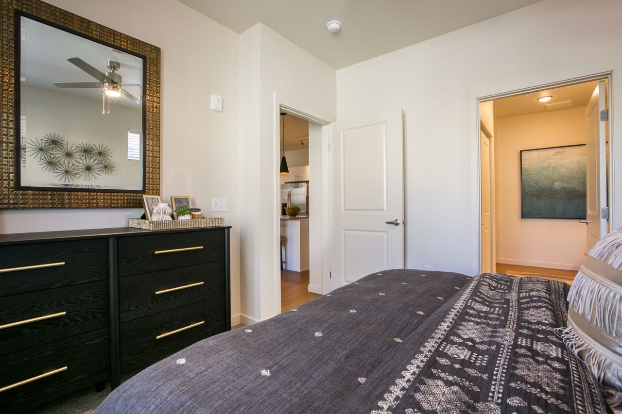Bedroom interior with a dark wood dresser, large mirror, and bed.