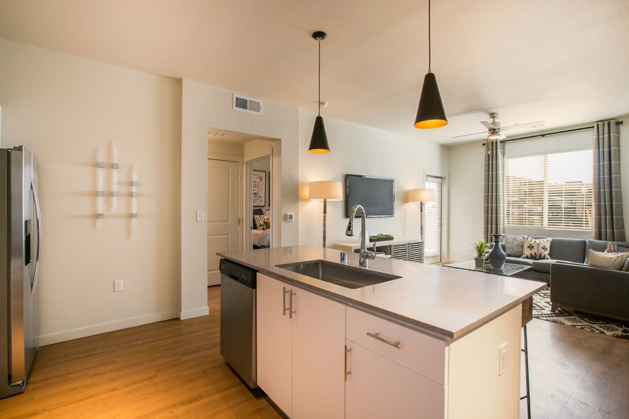 Open-concept apartment kitchen with island, stainless fridge, and living area with sofa and TV.