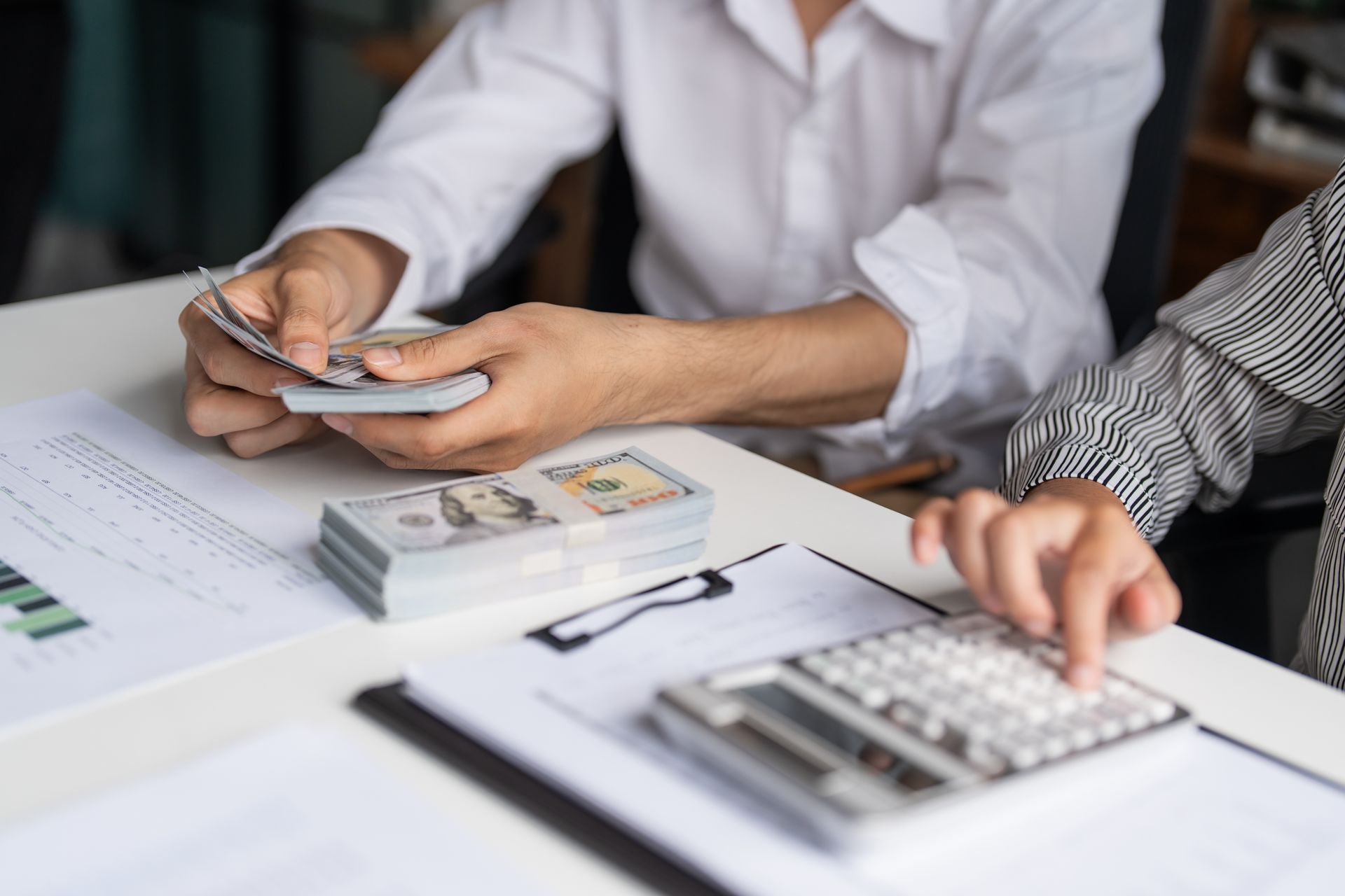 People counting cash and entering figures into a calculator at a desk with documents.