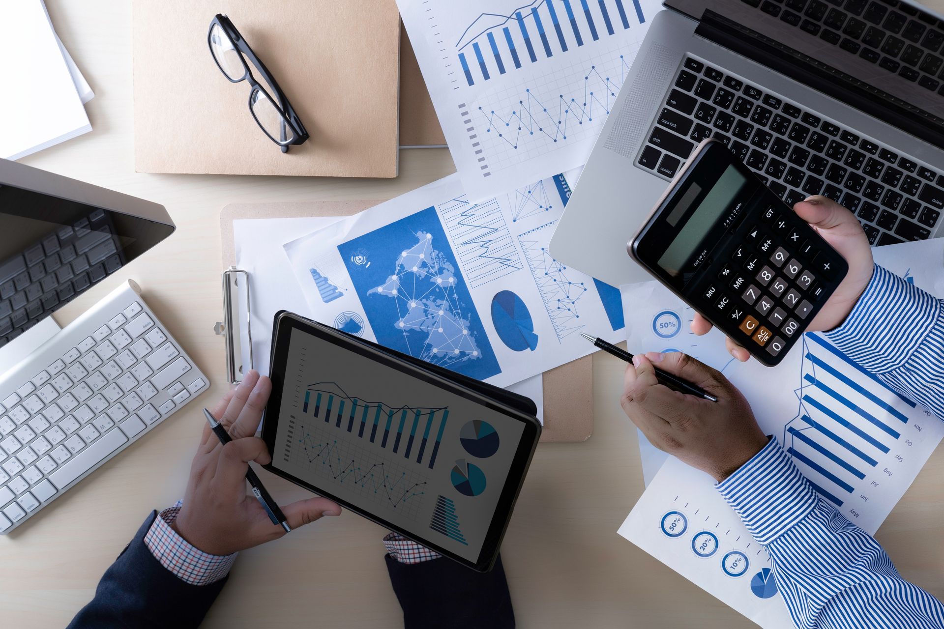 A workspace with two people analyzing financial charts and graphs on paper and a tablet.