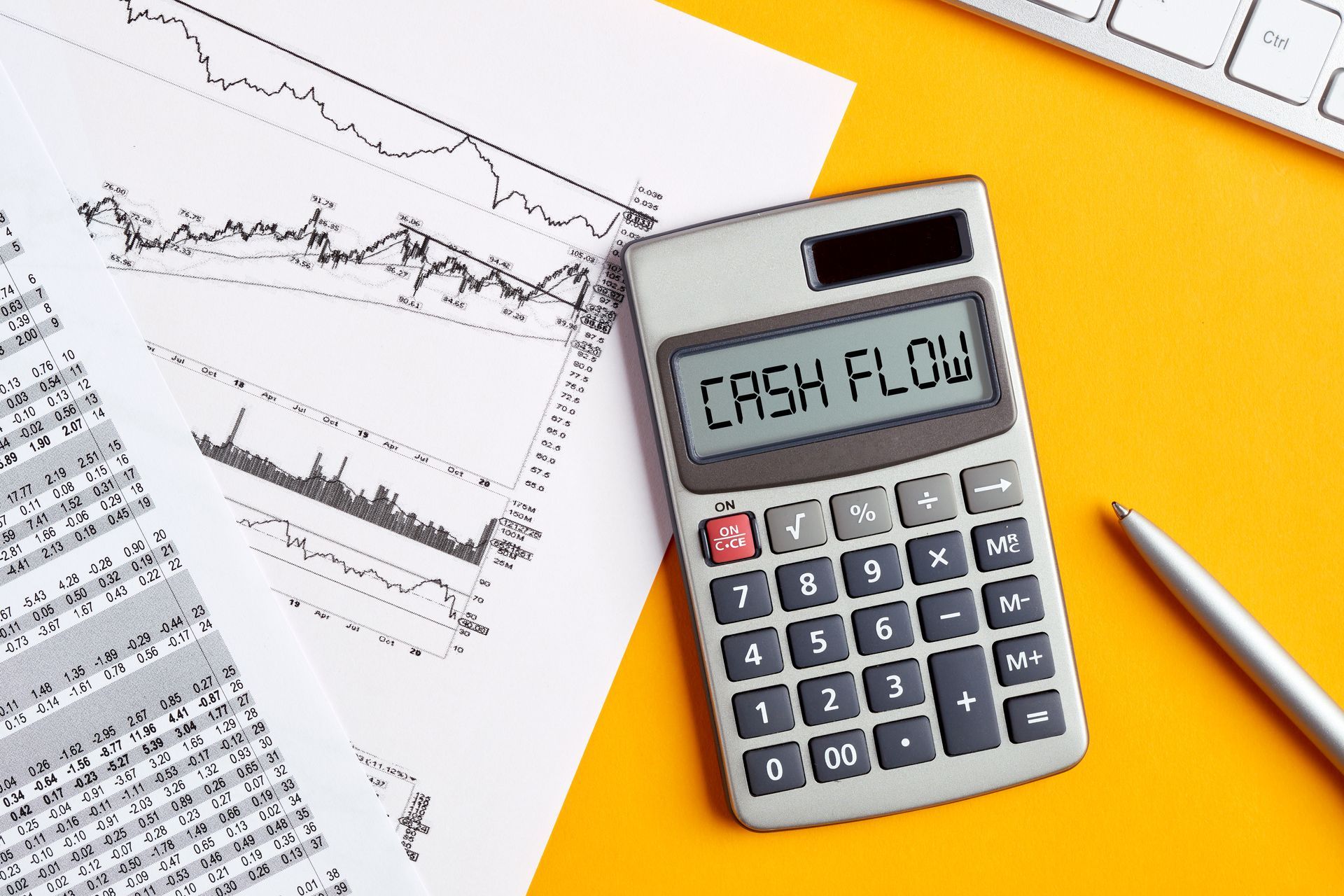 Calculator displaying “CASH FLOW” beside printed financial charts, graphs, and a pen on a desk.