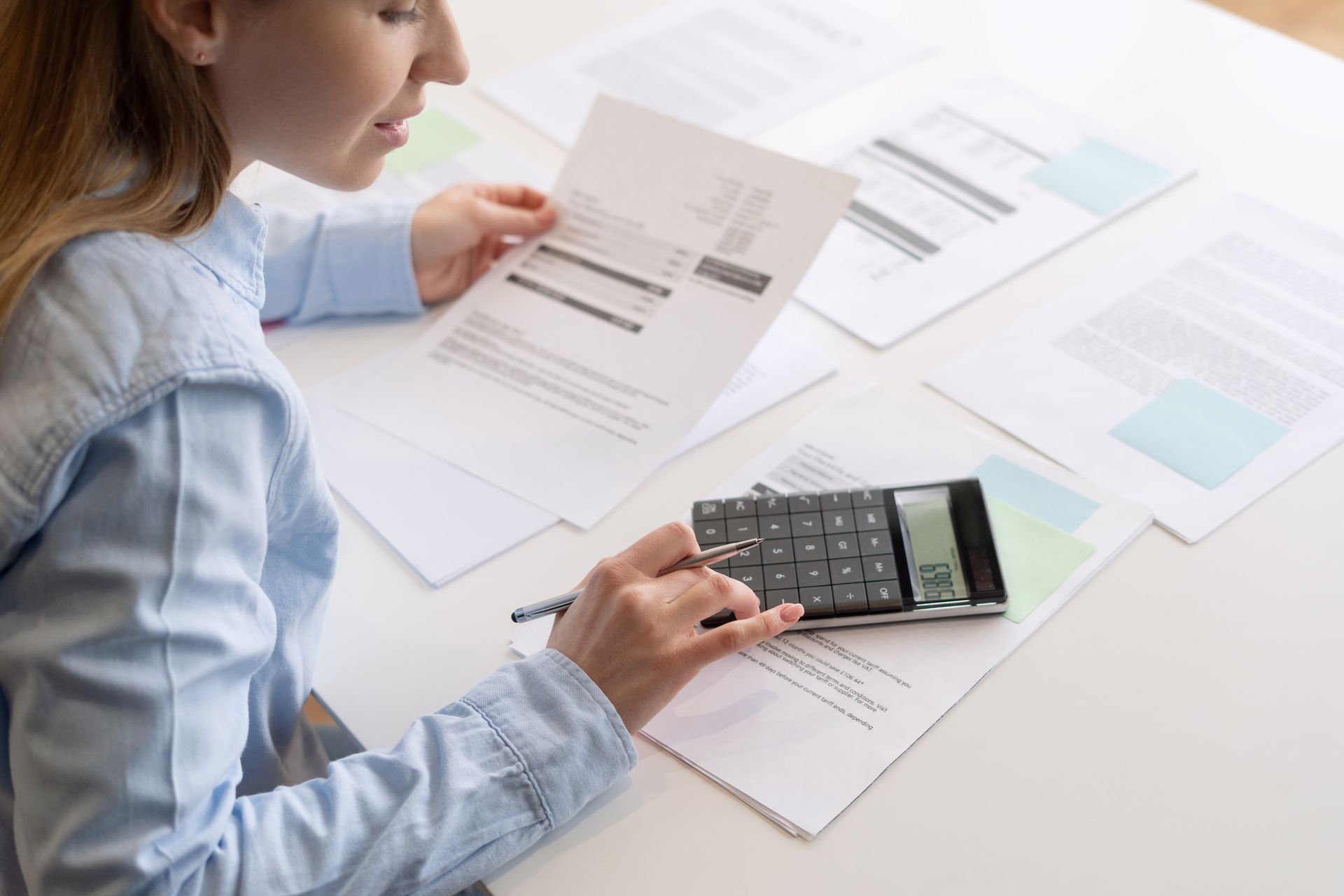 A woman small business owner is using a calculator and holding documents in her hands.