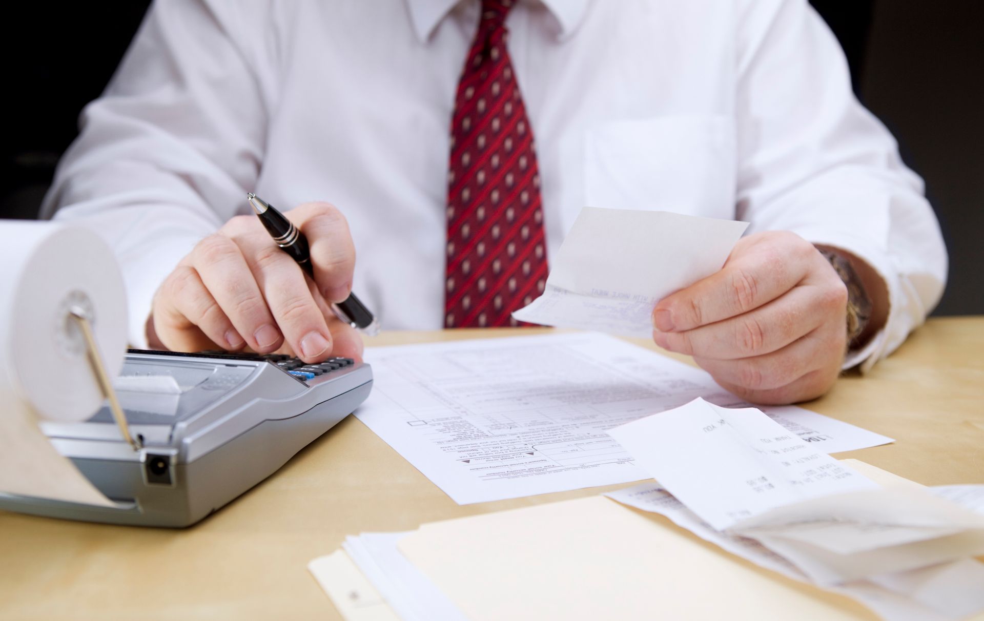 A male accountant is checking receipts and making calculations on a calculator.