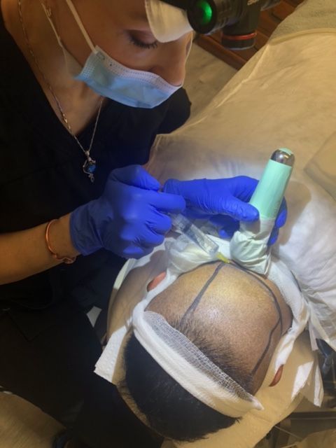 Two surgeons in blue scrubs and surgical masks perform a hair transplant procedure on a patient in a sterile clinic.