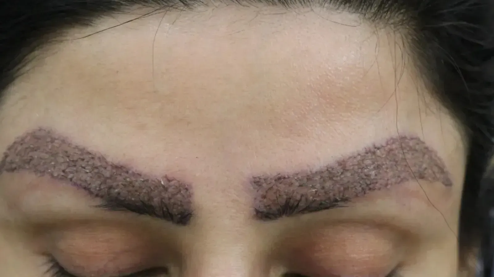 Close-up of a person's eyes and eyebrows; the eyebrows are dark and appear to be tattooed.