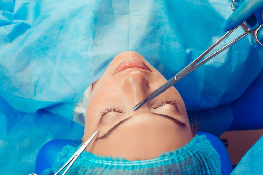 Woman undergoing a medical procedure; surgical tools near her nose, in a sterile environment.