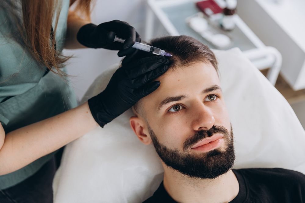 Person receiving scalp injections; a professional holds a syringe with black gloves.
