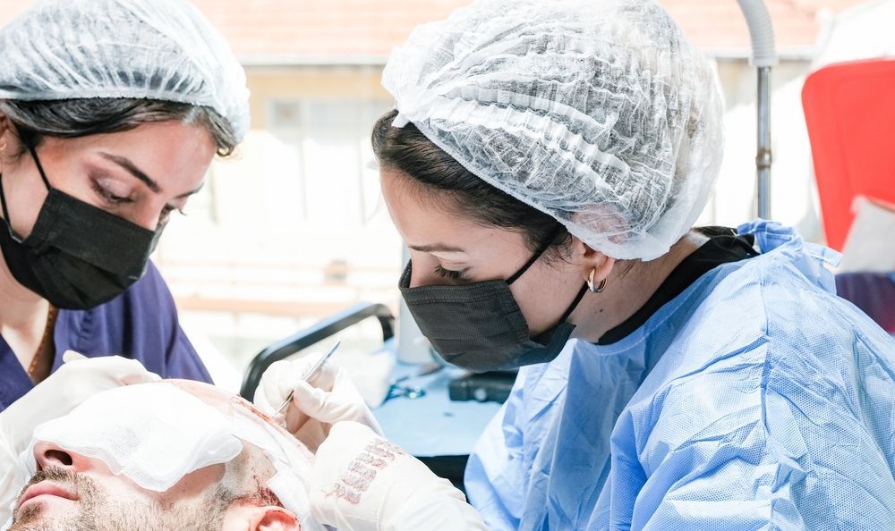 Two healthcare workers performing a procedure on a patient in a medical setting.