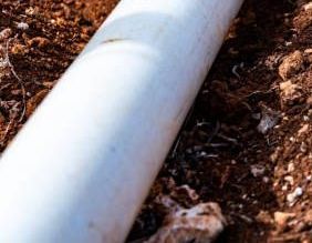 A man is fixing a pipe on a wall next to a red level.