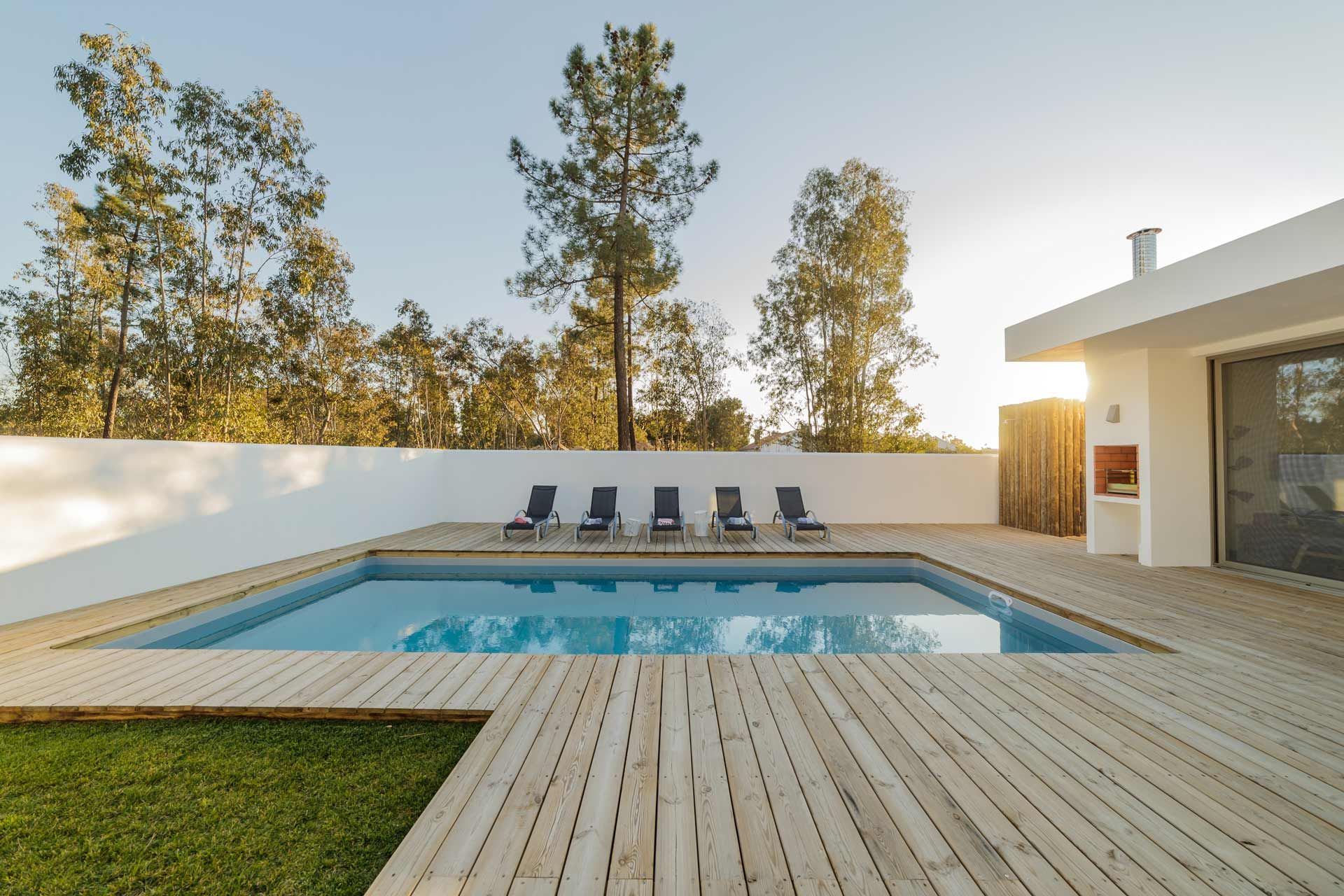 A large swimming pool with a wooden deck in front of a house.