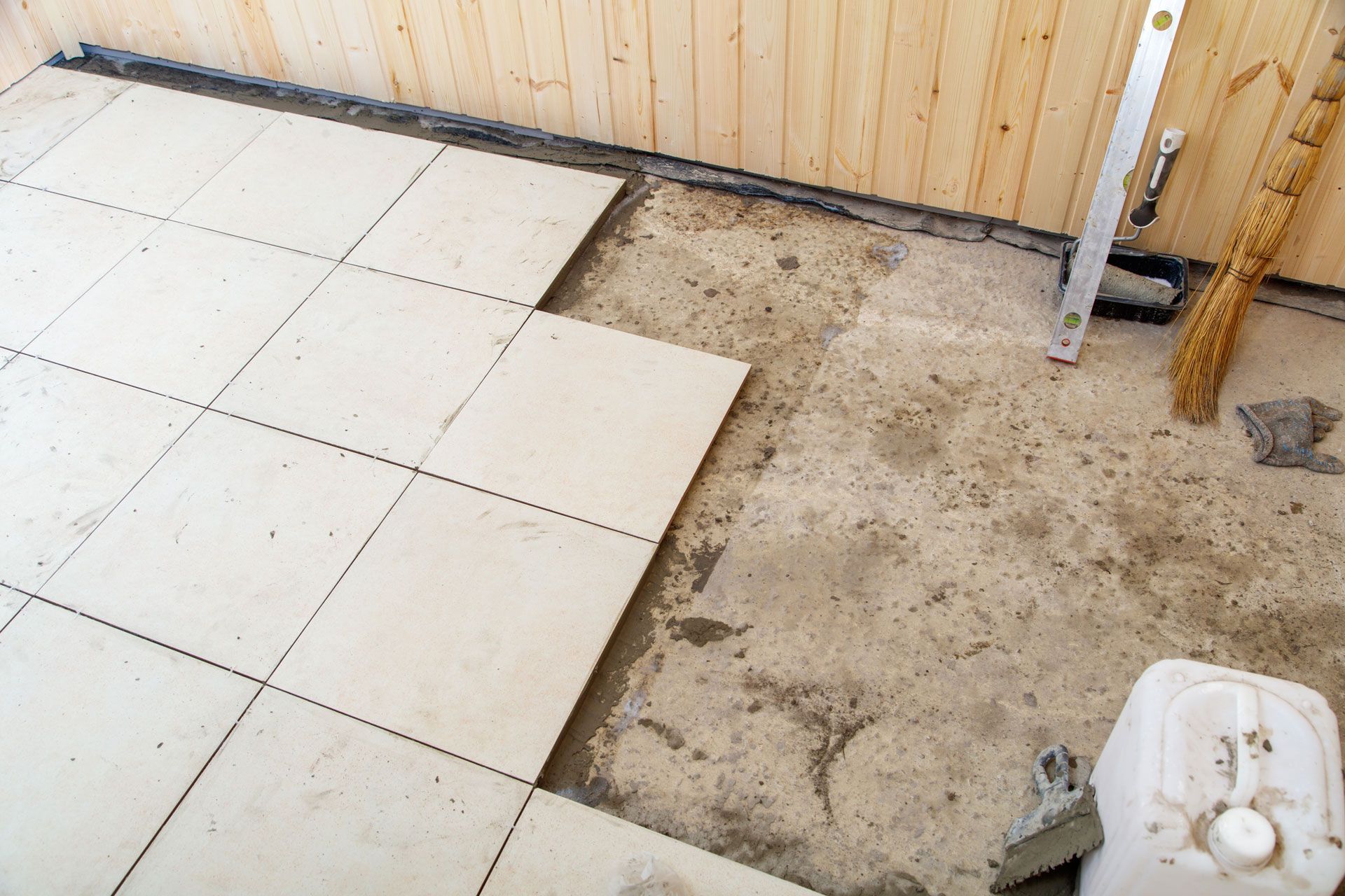 Tiled floor installation in progress: white tiles laid on cement; wood panel wall in background.