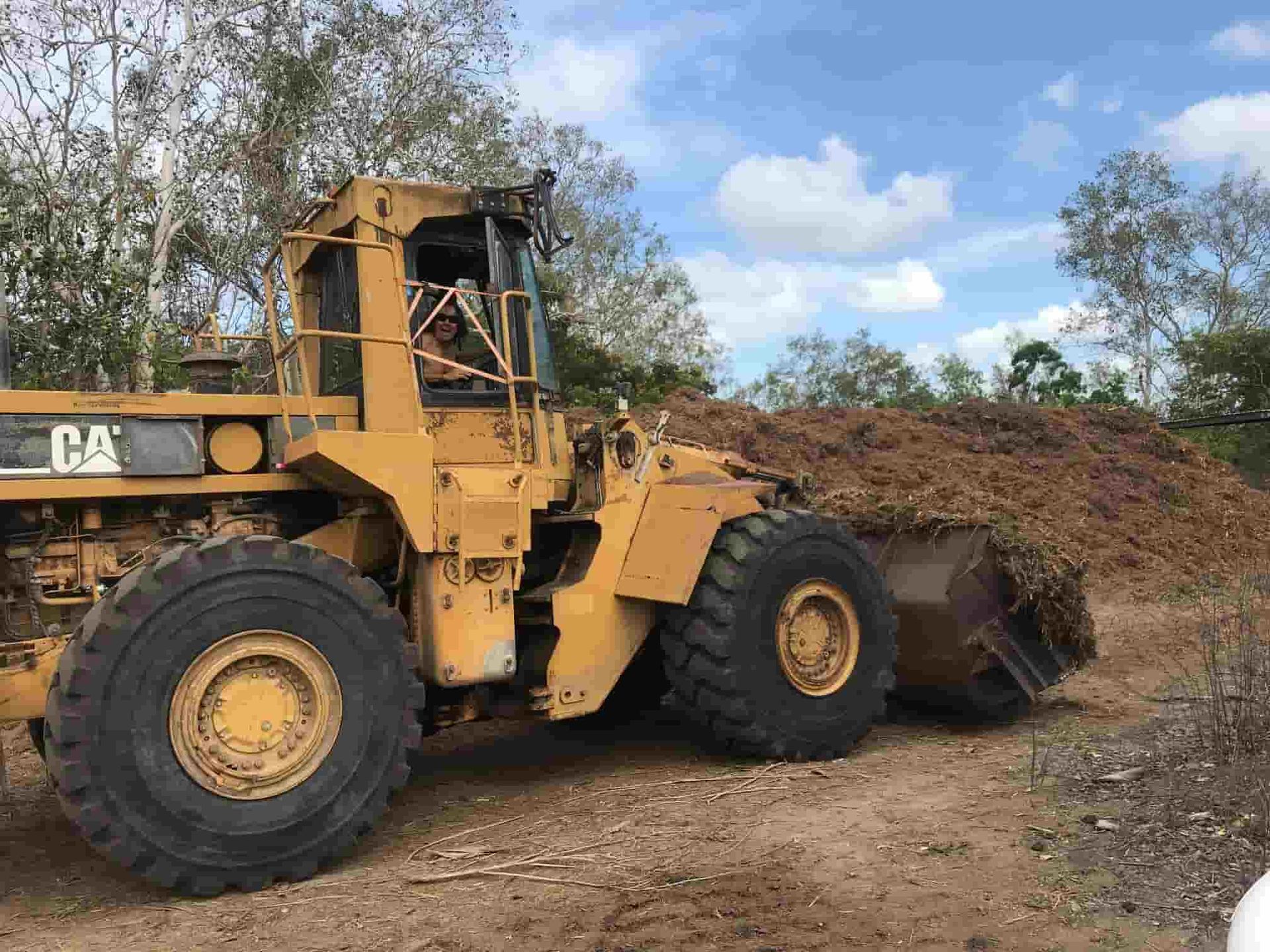 A Yellow Bulldozer Is Sitting In Front Of A Pile Of Wood — Chop N Chip Tree Fellas In Roseneath, QLD