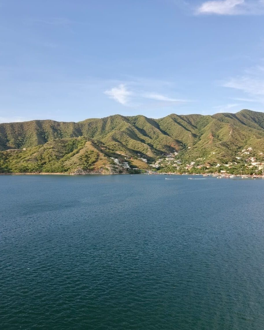 Una cascada cae sobre un terreno rocoso hasta formar una pequeña poza. Una exuberante vegetación rodea la cascada. Dos figuras nadan en la poza.