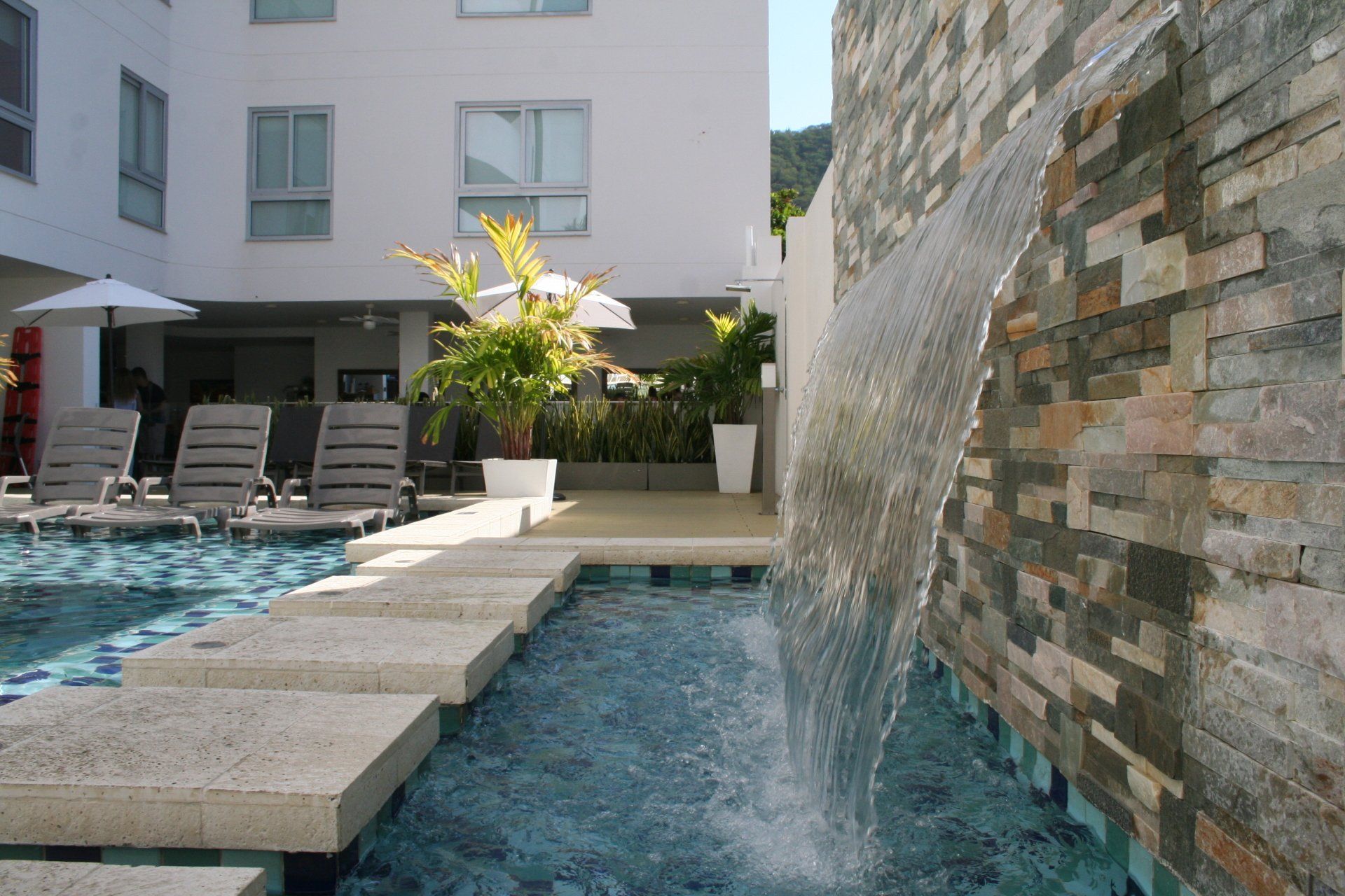 Una piscina con cascada al lado de un edificio con tumbonas y sombrillas.