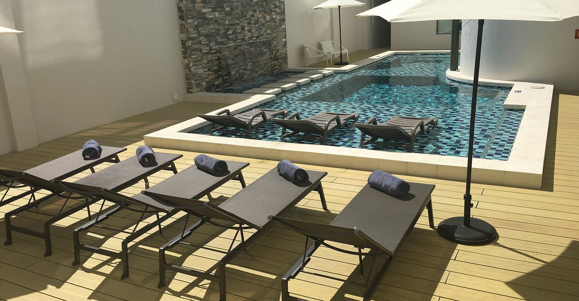Escena junto a la piscina con tumbonas, toallas, sombrillas y una pared texturizada.