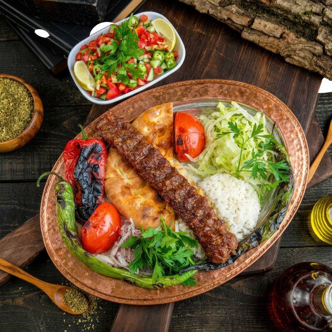Piatto di kebab grigliato con riso, verdure arrosto, insalata e salse su un tavolo di legno.