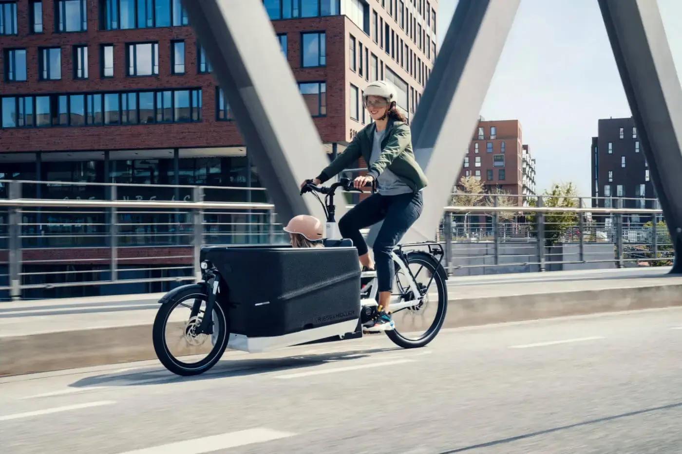 Eine Frau fährt mit einem Lastenfahrrad über eine Brücke.