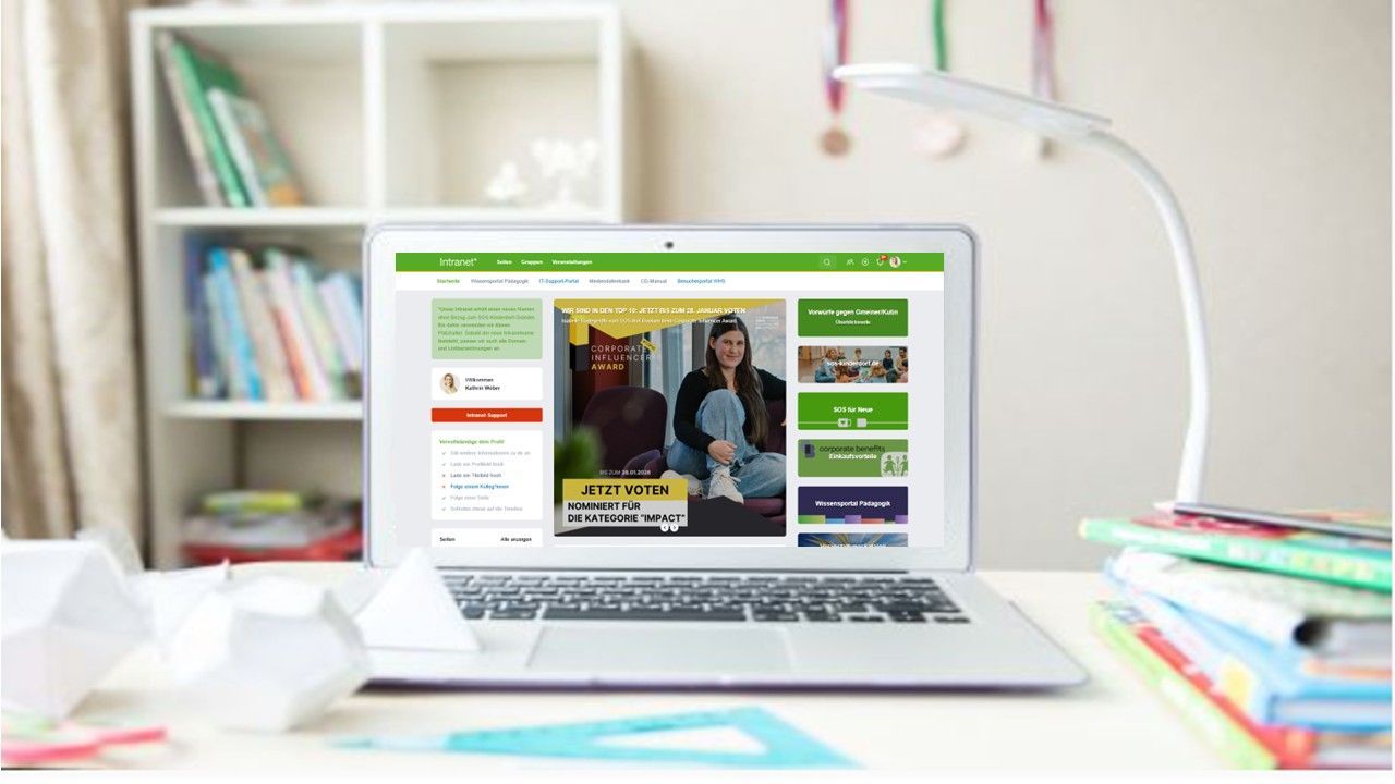 Schreibtisch mit vielen Unterlagen und in der Mitte heller Laptop mit Intranet-Startseite des SOS-Kinderdorf Intranet