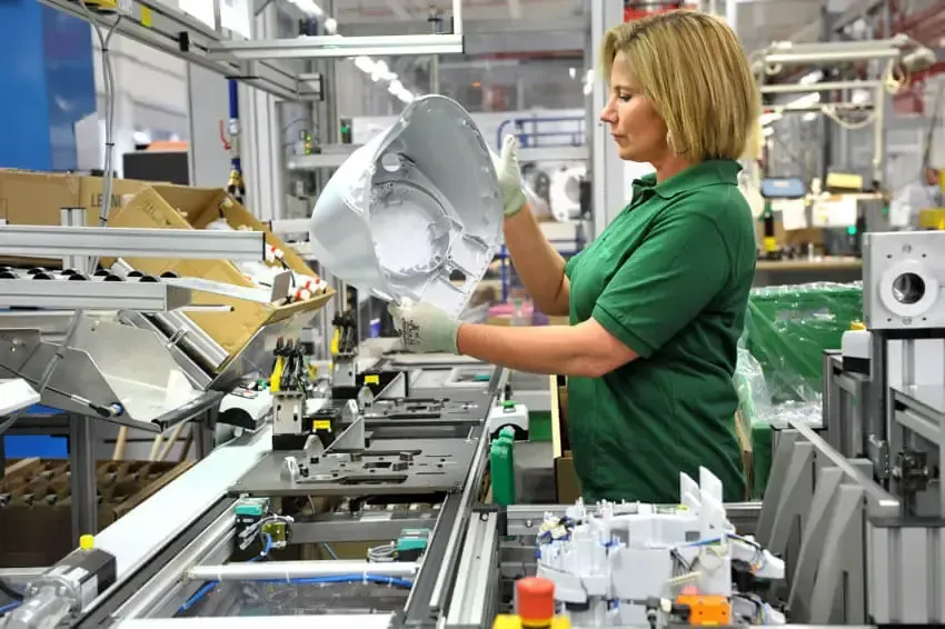 A woman in a green shirt is working in a factory.