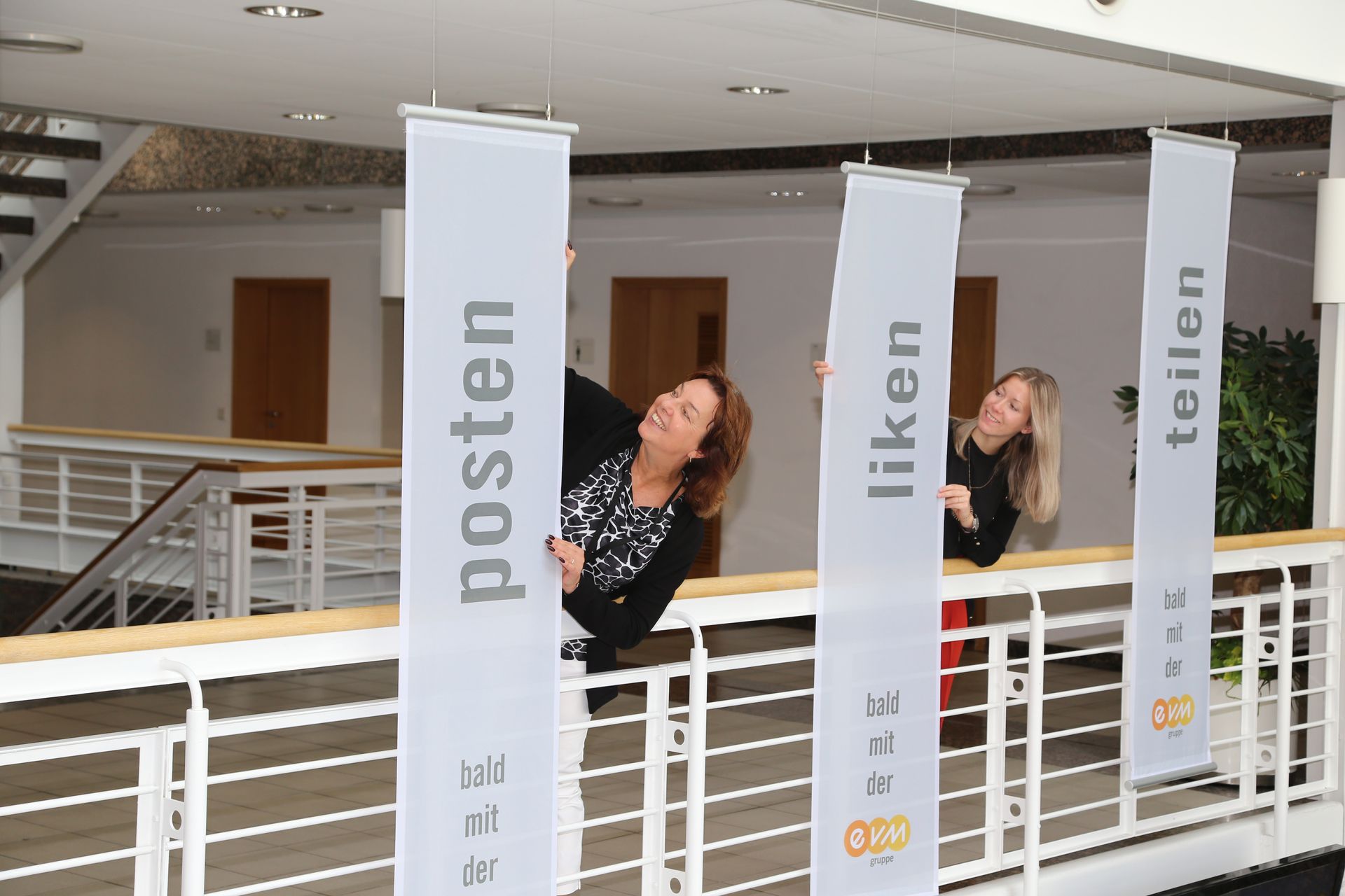 Zwei Frauen neben weißen vertikalen Bannern in einem Foyer bzw Galerie