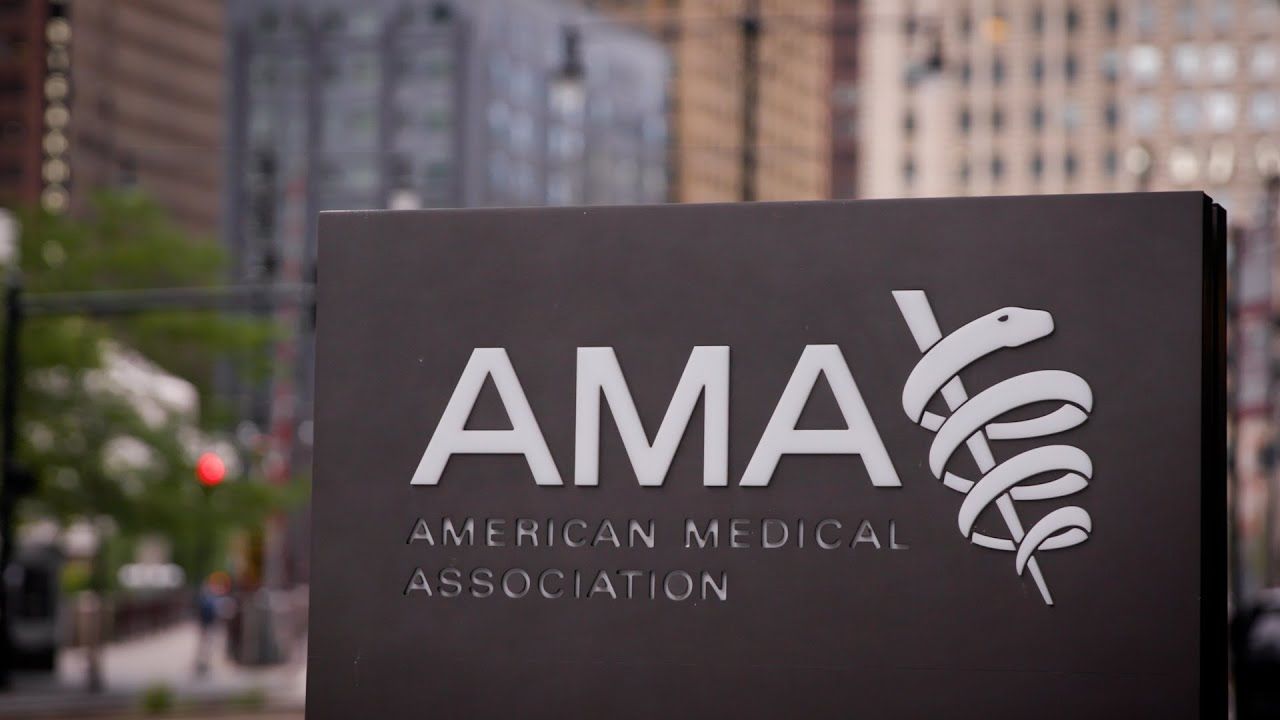 A sign for the american medical association is sitting in front of a city street.