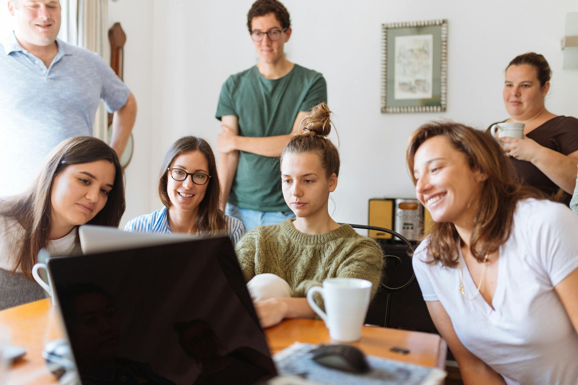 A group of people are sitting around a table looking at a laptop computer.