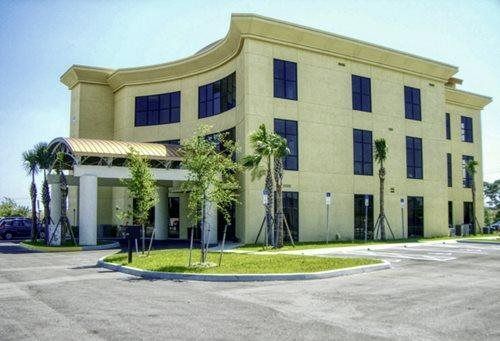 Cream-colored office building with palm trees and a curved entrance on a sunny day